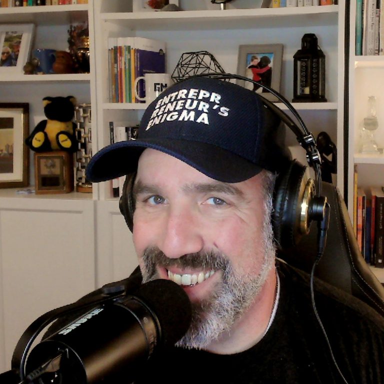 Seth Goldstein with Entrepreneur's Enigma baseball cap and a microphone. Smiling.