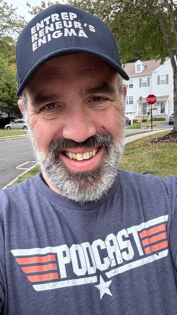 Seth out and about in his neighborhood wearing an Entrepreneur's Enigma hat and a Top Gun inspired t-shirt that says Podcast but looks like the Top Gun logo.